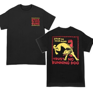 May include: Black t-shirts with the text "STICK TO YOUR GUNS" in red and yellow. One shirt has the text on the front and back, and the other has the text on the front only. The back of the shirt features a yellow dog graphic.