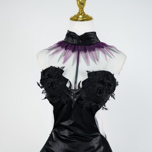 May include: A black satin dress with a high collar and a sheer, purple-trimmed neckline. The bodice features intricate black lace detailing. The dress is displayed on a mannequin with a gold-colored stand.