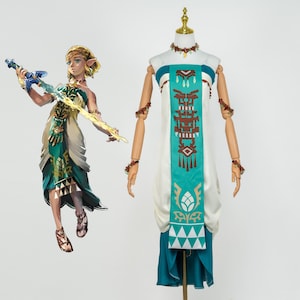 Op de afbeelding: Een cosplaykostuum van een personage uit een videogame. Het kostuum is wit, blauwgroen en bruin, met ingewikkelde patronen. Een beeldje van het personage houdt een zwaard vast. Het kostuum wordt op een mannequin getoond.