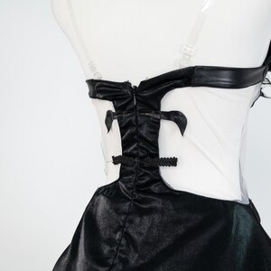 May include: A black and white dress with a fitted bodice and flared skirt. The bodice features a black, shiny fabric with decorative accents and a sheer white panel. The dress has a high neckline and a defined waistline, creating a classic silhouette.