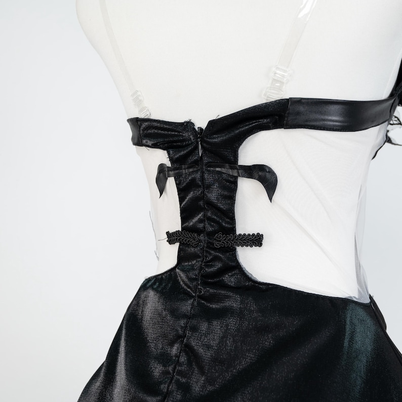 May include: A black and white dress with a fitted bodice and flared skirt. The bodice features a black, shiny fabric with decorative accents and a sheer white panel. The dress has a high neckline and a defined waistline, creating a classic silhouette.