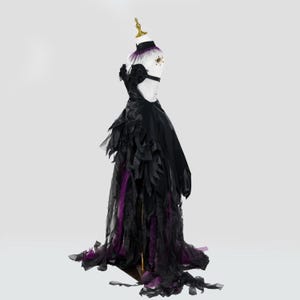 May include: A black formal gown with a high collar and open back, displayed on a mannequin. The dress features layered, feathery accents in black and purple, with a long train. The mannequin has a gold-colored headpiece.