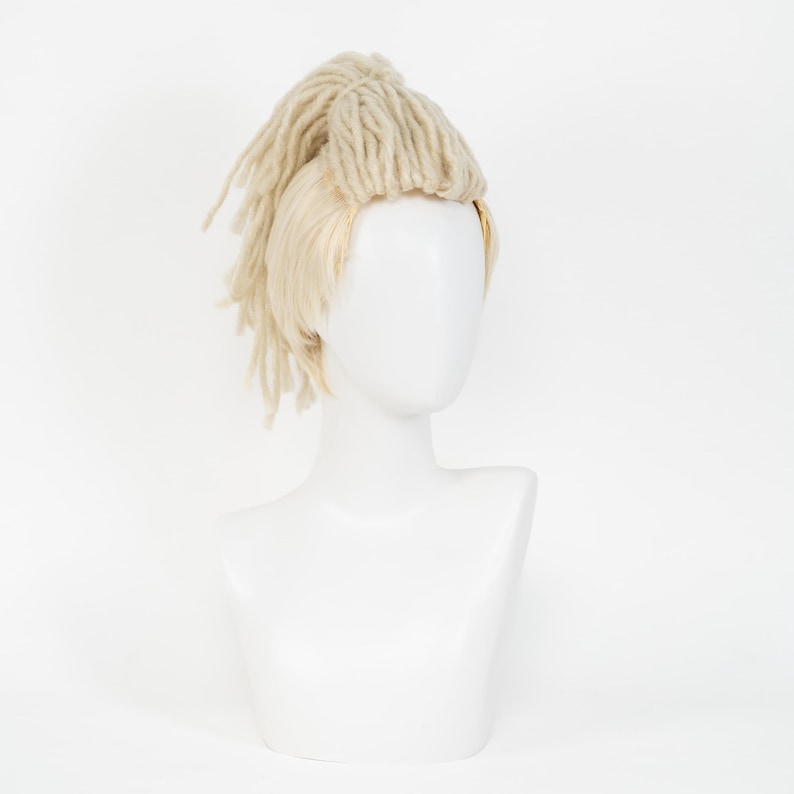 May include: A blonde wig with dreadlocks and straight hair. The wig is displayed on a white mannequin head and shoulders. The dreadlocks are a light beige color, and the straight hair is a lighter blonde.