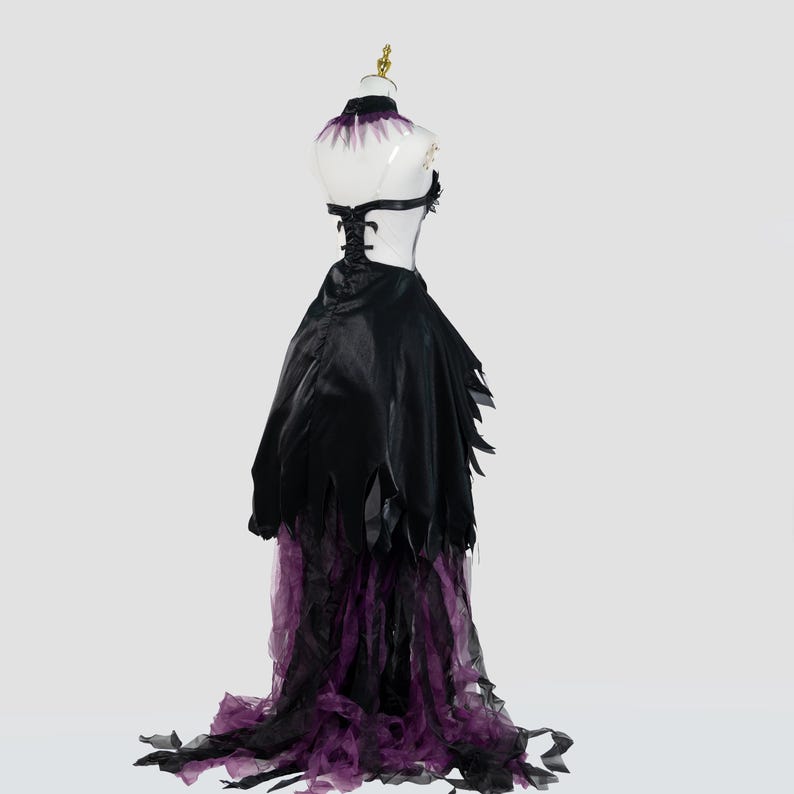 May include: A black and purple costume dress on a mannequin. The dress features a black bodice with a halter neck and a flowing skirt with tattered edges. The skirt transitions to a purple tulle hem. The mannequin has a gold-colored head.