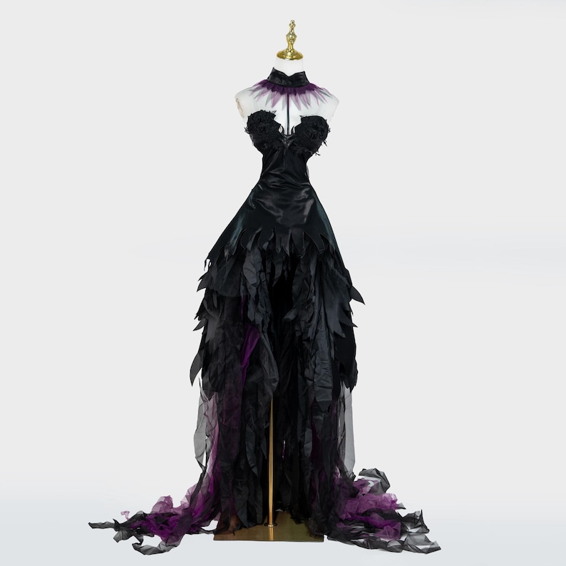 May include: A black formal gown with a high collar and a flowing skirt. The bodice is strapless and adorned with black fabric. The skirt features layers of black and purple fabric, creating a dramatic effect. The dress is displayed on a mannequin.