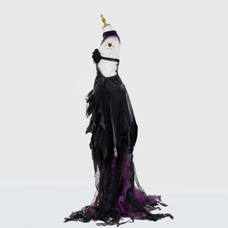 May include: A black and purple gothic-style dress on a mannequin. The dress features a halter top, a black skirt with tattered edges, and a flowing train with purple accents. The mannequin has a gold-colored head.