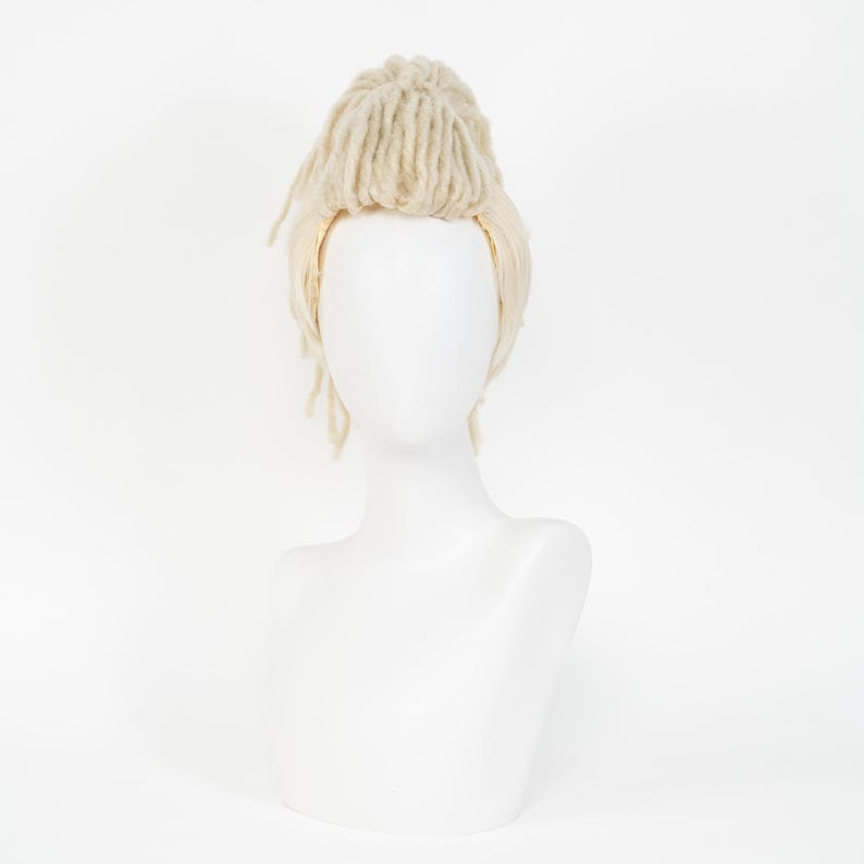 May include: A light blonde wig with dreadlock-style strands and a bun on top, displayed on a white mannequin head. The wig has a natural-looking texture and color, suitable for cosplay or costume use.
