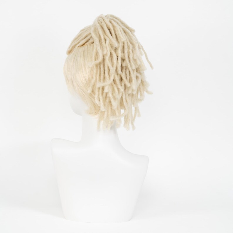 May include: A mannequin head displaying a light blonde wig with a section of cream-colored dreadlocks. The wig is styled with the dreadlocks gathered at the crown of the head. The mannequin is white, and the background is plain white.