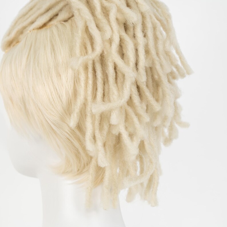 May include: A light blonde wig with a combination of straight hair and dreadlock-style extensions. The wig is styled to cover the top and back of the head, with the dreadlocks cascading down the back. The hair is a light, natural blonde color.