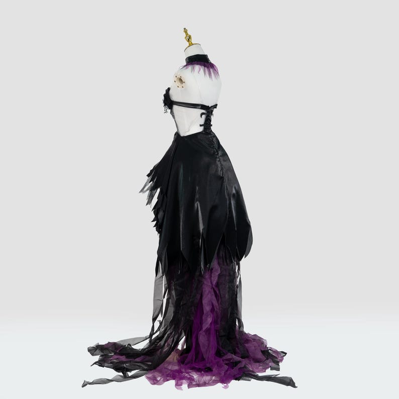 May include: A black and purple costume dress displayed on a mannequin. The dress features a black bodice with a lace-up back and a flowing skirt with tattered edges. The skirt transitions to a purple, layered, sheer fabric at the hem.