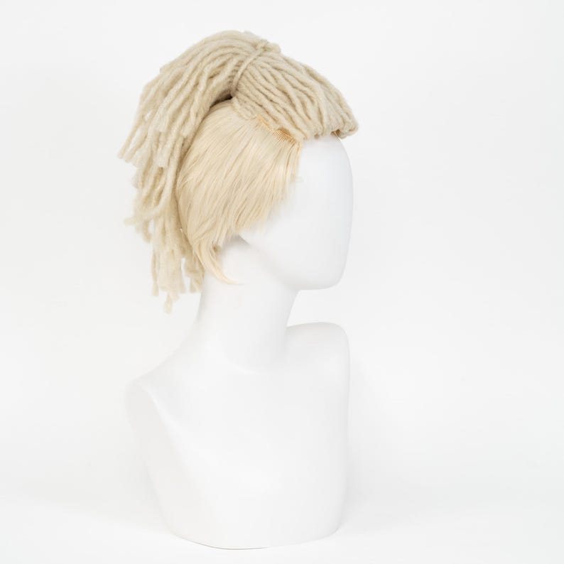 May include: A mannequin head displaying a light blonde wig with a combination of straight and dreadlock-style hair. The dreadlock section is a lighter shade of blonde and is styled on top of the head.