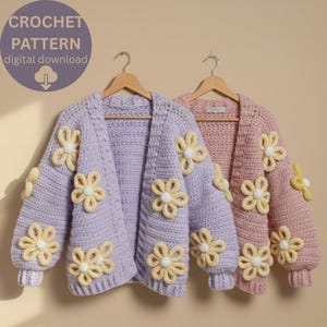 Könnte beinhalten: Zwei gehäkelte Strickjacken, eine in Lavendel und eine in Rosa, jeweils mit gelben und weißen Blumenapplikationen verziert. Die Strickjacken werden auf Holzbügeln präsentiert. Das Bild enthält den Text "CROCHET PATTERN digital download".