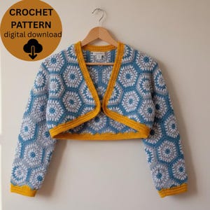 May include: A crocheted bolero with a geometric pattern in shades of blue, gray, and white, trimmed with yellow. The garment is displayed on a wooden hanger. Text on the image reads "CROCHET PATTERN digital download".
