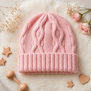 May include: A light pink knit beanie featuring a vertical cable knit pattern on the main body and a wide ribbed cuff at the base. The hat is constructed from a soft yarn material and displays a consistent pastel pink color throughout the design.