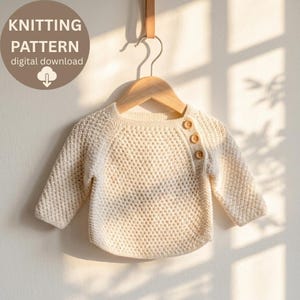 Puede incluir: Suéter de bebé tejido de color crema con mangas largas y tres botones de madera en el hombro. El suéter está colgado de una percha de madera. La imagen incluye el texto "KNITTING PATTERN digital download".