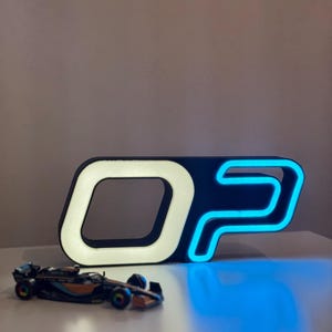 May include: A black and white illuminated sign with the letters "OP" in a stylized font, with a blue neon outline. A small, detailed model race car is in front of the sign.