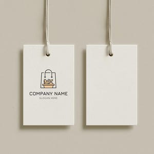 Könnte beinhalten: Zwei weiße rechteckige Anhänger mit einer Schnur oben. Der linke Anhänger zeigt ein Einkaufstaschen-Logo mit Brot und anderen Artikeln sowie den Text "COMPANY NAME" und "SLOGAN HERE". Der rechte Anhänger ist leer.