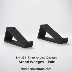 May include: A pair of small 115mm black angled desktop stand wedges. These triangular supports feature a matte finish with a small lip at the front edge to hold items securely. The text "Small 115mm Angled Desktop Stand Wedges — Pair" is visible.