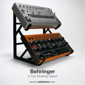Puede incluir: Un soporte de escritorio negro de 2 niveles que sostiene dos sintetizadores plateados y naranjas. El soporte es de metal negro y tiene el texto "Behringer 2-Tier Desktop Stand" en la parte inferior.