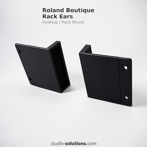 May include: Two black Roland Boutique Rack Ears, designed for desktop or rack mount use. Each ear has a right-angle shape with pre-drilled holes for mounting. The text "Roland Boutique Rack Ears" and "Desktop / Rack Mount" is visible.