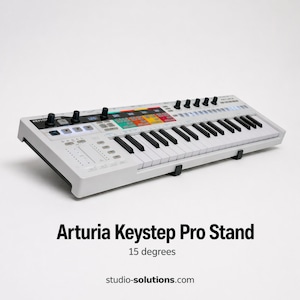 May include: A white Arturia Keystep Pro Stand with black keys and controls. The stand has a colorful section with various buttons and knobs. The text "Arturia Keystep Pro Stand" is displayed below the stand, along with "15 degrees" and "studio-solutions.com".