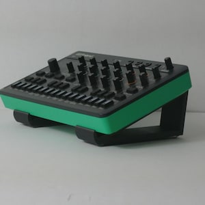 Könnte beinhalten: Ein schwarzes und grünes elektronisches Musikproduktionsgerät mit zahlreichen Knöpfen und Reglern. Das Gerät ist auf einem schwarzen Ständer montiert. Das Gerät hat einen grünen Rand und ist für die Musikproduktion und Klangbearbeitung konzipiert.