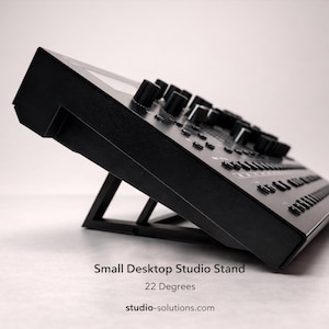 May include: A black desktop studio stand angled at 22 degrees, designed for audio equipment. The stand has a minimalist design with a sturdy base, suitable for small studio setups. The stand is made of durable materials.