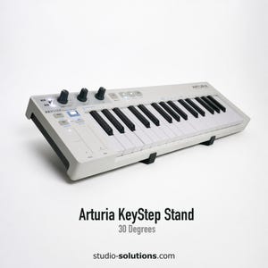 May include: A white Arturia KeyStep stand with black keys and control knobs. The stand is angled at 30 degrees and has the text "Arturia KeyStep Stand" and "30 Degrees" printed on it.
