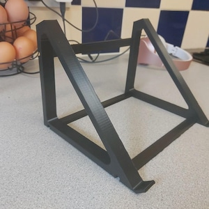 May include: A black laptop stand with a geometric design. The stand is made of a solid material and features angled supports and a base to hold a laptop. The stand is designed to elevate a laptop for better ergonomics.