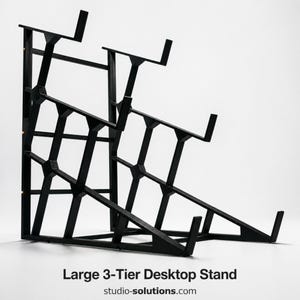 May include: A black, three-tiered desktop stand with a geometric design. The stand is made of metal and has a sturdy construction. The text "Large 3-Tier Desktop Stand" and the website address "studio-solutions.com" are visible.