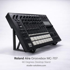 Op de afbeelding: Een zwarte Roland Aira Groovebox MC-707 muziekproductiewerkstation gemonteerd op een zwarte desktopstandaard met een hoek van 60 graden. Het apparaat is voorzien van een raster van witte pads, meerdere zwarte knoppen, schuifregelaars en een digitaal scherm.