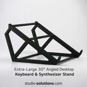 Peut inclure: Un support de bureau noir, extra-large, incliné à 30 degrés pour clavier et synthétiseur, doté d'une structure géométrique. Le texte "Extra-Large 30° Angled Desktop Keyboard & Synthesizer Stand" et "studio-solutions.com" est imprimé en dessous.