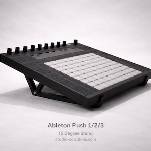 May include: A black stand for an Ableton Push 1/2/3, angled at 15 degrees. It has a grid of white squares and black buttons. The text "Ableton Push 1/2/3" and "15 Degree Stand" are visible.