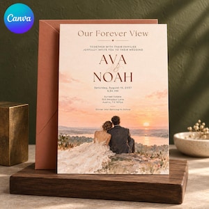 May include: A wedding invitation card featuring the text Our Forever View, Ava and Noah, and event details. The design displays a painted sunset landscape with a couple sitting on a rock overlooking a lake, paired with a solid terracotta envelope.