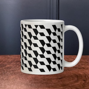 May include: White ceramic mug with a black and white geometric pattern. The design features repeating black diamond shapes against a white background. The mug has a curved handle and is set on a wooden surface.
