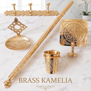 Peut inclure: Un ensemble d'accessoires de salle de bain en laiton comprenant une barre porte-serviettes, un porte-savon avec plaque ornée, un porte-savon mural carré, un gobelet et une patère à trois crochets. Chaque pièce présente des gravures. Texte : BRASS KAMELIA.