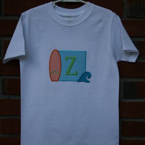 May include: White t-shirt with an embroidered design of a surfboard, a wave, and the letter "Z" in green.