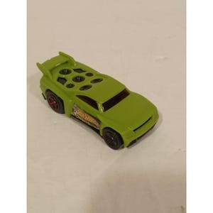 May include: A lime green Hot Wheels toy car featuring a rear spoiler, black wheels with red rims, and a series of circular cutouts on the roof. The side of the vehicle displays a Hot Wheels logo graphic with a soccer ball icon near the front wheel.