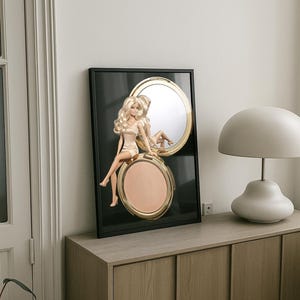 Peut inclure: Une impression d'art murale encadrée représentant une poupée blonde en robe claire assise sur le bord d'un poudrier doré ouvert. Le poudrier présente un miroir circulaire sur le couvercle et une poudre compacte beige clair sur la base.