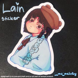 May include: A die-cut sticker featuring an anime-style character with short dark hair, large eyes, and a brown beret, wearing a light blue collared shirt. The text 'Lain' and 'Sticker' appear in the top left, with 'moesociety' in the bottom right corner.