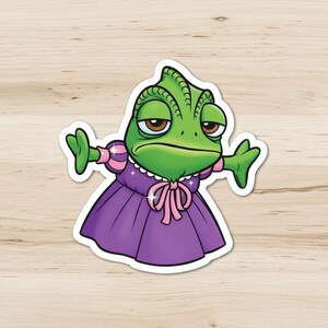 May include: A green chameleon sticker wearing a purple dress with a pink bow. The chameleon has a grumpy expression and is spreading its arms. The sticker is on a light wood grain surface.