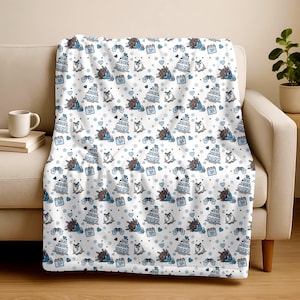 以下が含まれることがあります： 青いウェディングケーキ、花束、ハート、雪の結晶、カレンダーの繰り返し模様が施された白いブランケット。ベージュのソファに掛けられており、居心地が良く装飾的な外観を作り出しています。