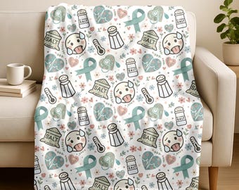 May include: White throw blanket with a repeating pattern of cartoon faces, salt shakers, thermometers, hearts, flowers, and teal ribbons. The word "SALT" is printed on some of the objects. The blanket is draped over a white sofa.