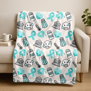 May include: A white throw blanket featuring a repeating pattern of teal and black cartoon graphics. The design includes salt shakers, thermometers, hearts with a heartbeat line, awareness ribbons, and a face with sweat drops.