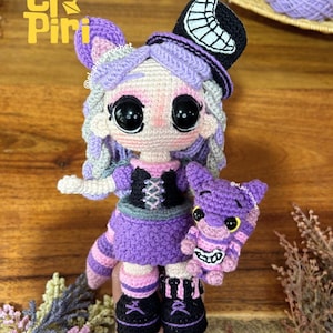 Puede incluir: Una muñeca tejida a mano con cabello violeta claro, grandes ojos negros y un sombrero de copa negro con una luna creciente blanca. La muñeca viste un vestido negro y violeta con corpiño acordonado, botas negras y sostiene una pequeña criatura rayada.