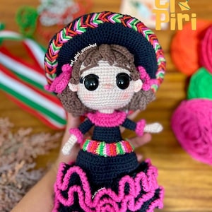 Puede incluir: Muñeca de ganchillo hecha a mano con un vestido negro con una falda con volantes rosas y un cinturón bordado colorido. La muñeca tiene un sombrero azul oscuro con adornos coloridos y detalles rosas. Los ojos de la muñeca son grandes y negros. El texto "El Piri" es visible.