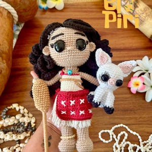 Puede incluir: Muñeca de ganchillo hecha a mano de una princesa polinesia con cabello oscuro, una falda roja y un perro blanco pequeño. La muñeca sostiene una paleta beige. El texto "El Piri" es visible en la esquina superior derecha.
