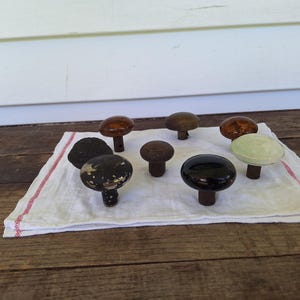 May include: A collection of antique door knobs in various colors and finishes, including brown, black, and green. The knobs are arranged on a white cloth with red trim, set against a rustic wooden surface.