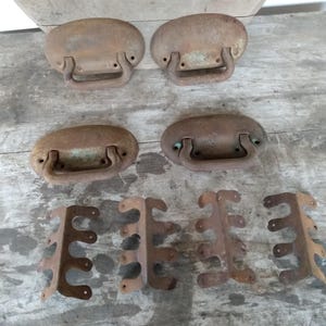 May include: Four rusty metal handles with oval-shaped plates and a metal loop for pulling.  Three rusty metal brackets with five holes each.
