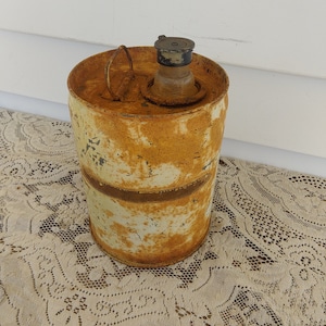 May include: A rusty metal container with a lid and a white background. The container is sitting on a white lace tablecloth.